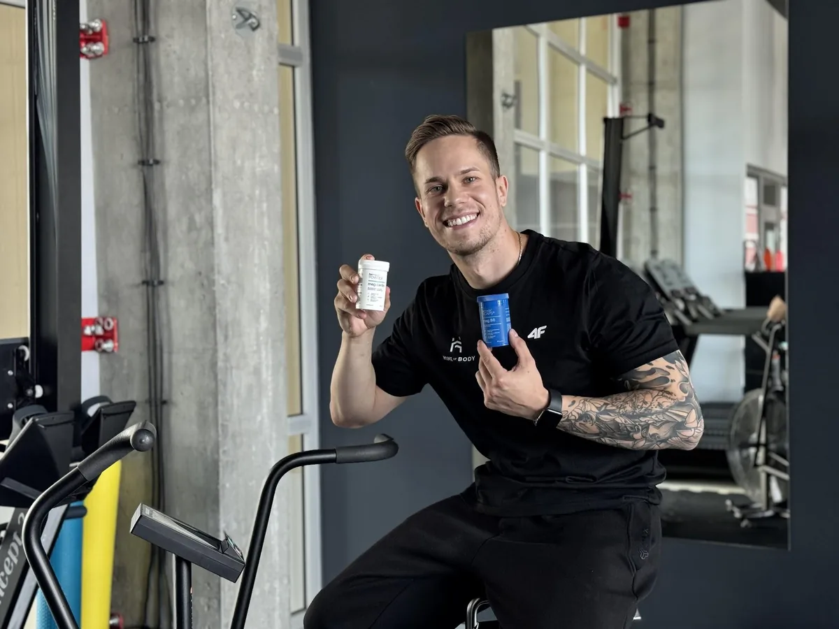 Adrian Domagalski trzyma ForMeds Mag Cardio w proszku i Bicaps Mag B6 w kapsułkach na siłowni