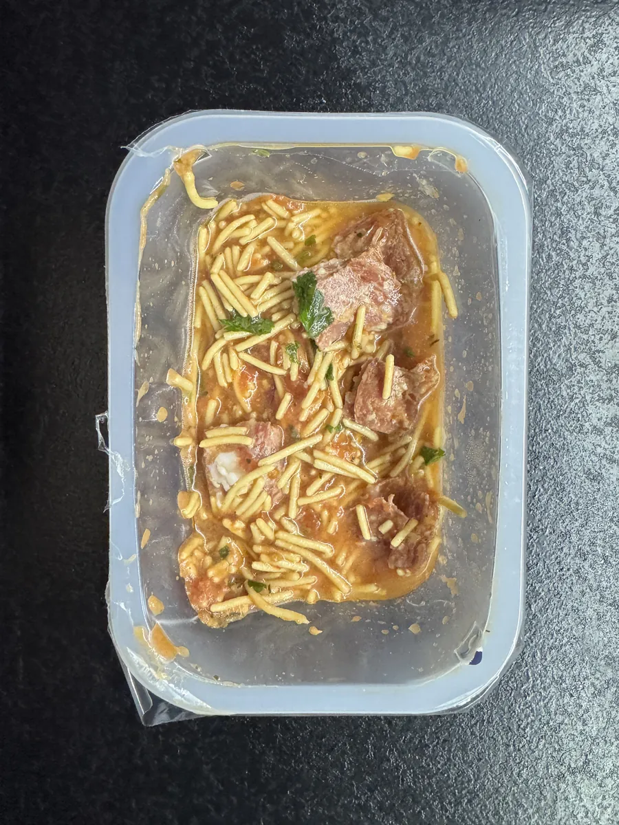 Otwarte pudełko 5PD ze spaghetti all'assassina, na krawędzi zostały strzępy folii ochronnej