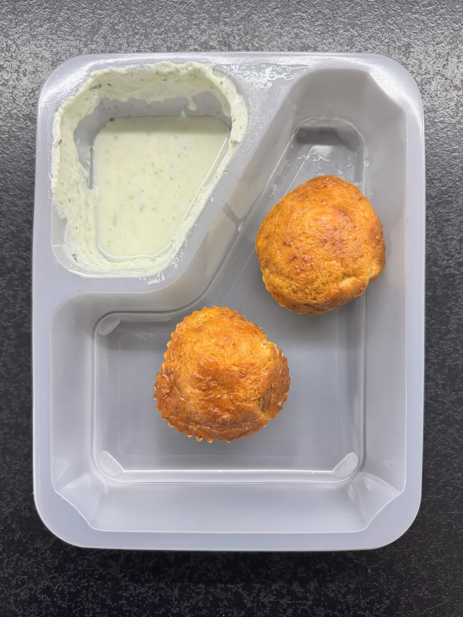 Otwarte pudełko AfterFit: dwie muffiny cukiniowo-pomidorowe i osobna porcja sosu jogurtowo-ziołowego