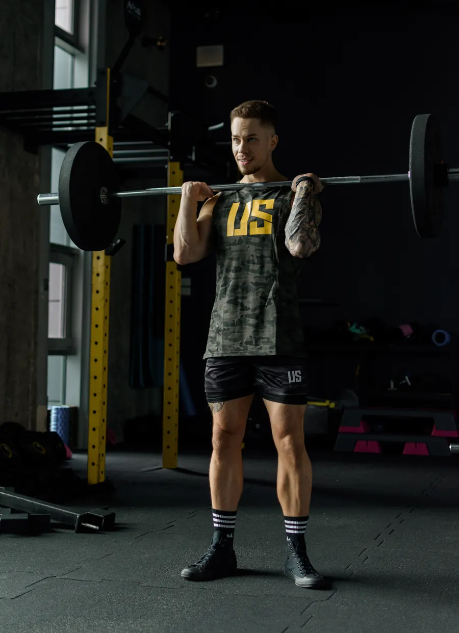 Adrian Domagalski w tank topie Make Us Strong moro trzyma sztangę w pozycji front rack